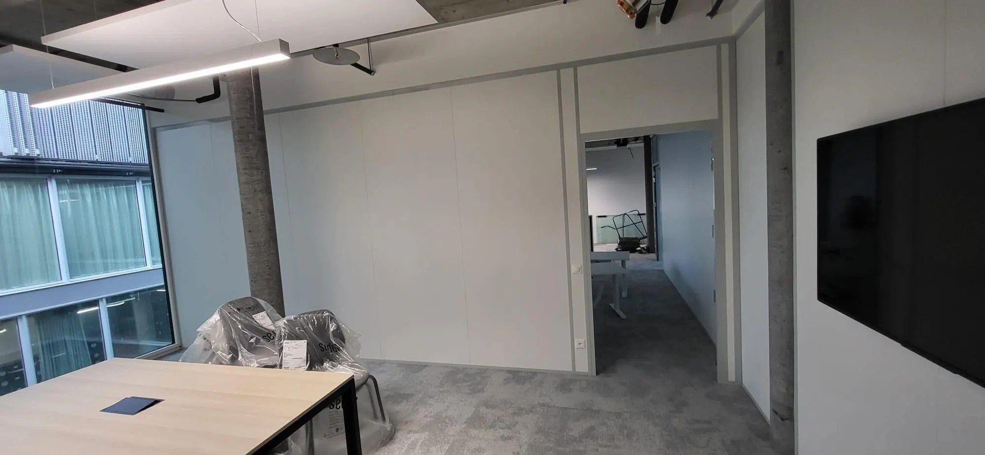 Weisse Vollwand-Systemtrennwand mit Tür vor einem Sitzungszimmer mit Bildschirm