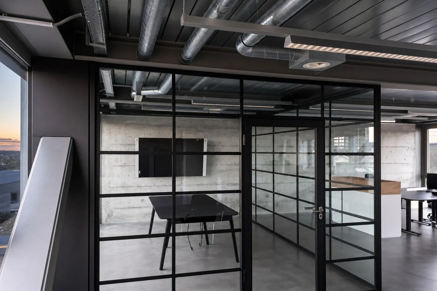 Loft-Glaswand mit schwarzem Sprossenraster und Tür neben einem Sitzungstisch