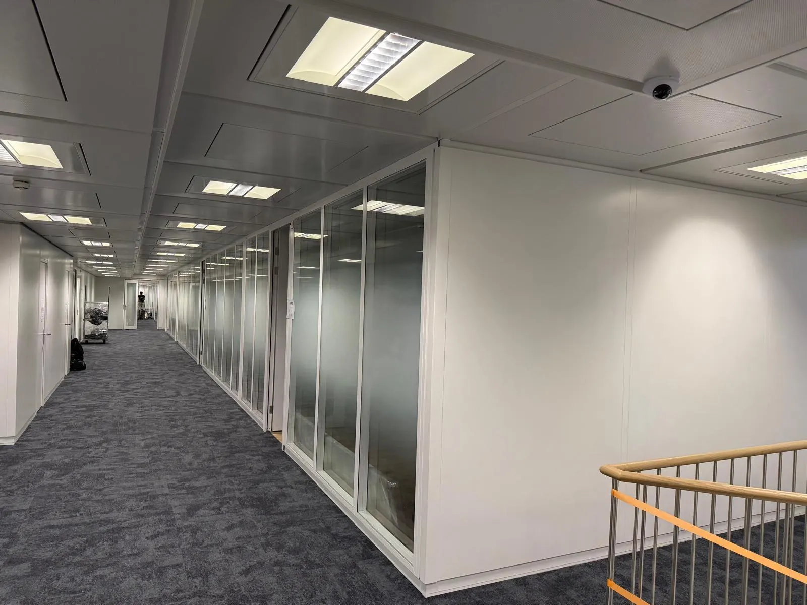 Korridor mit Systemtrennwand aus Glas und Vollwand neben einem Treppengeländer